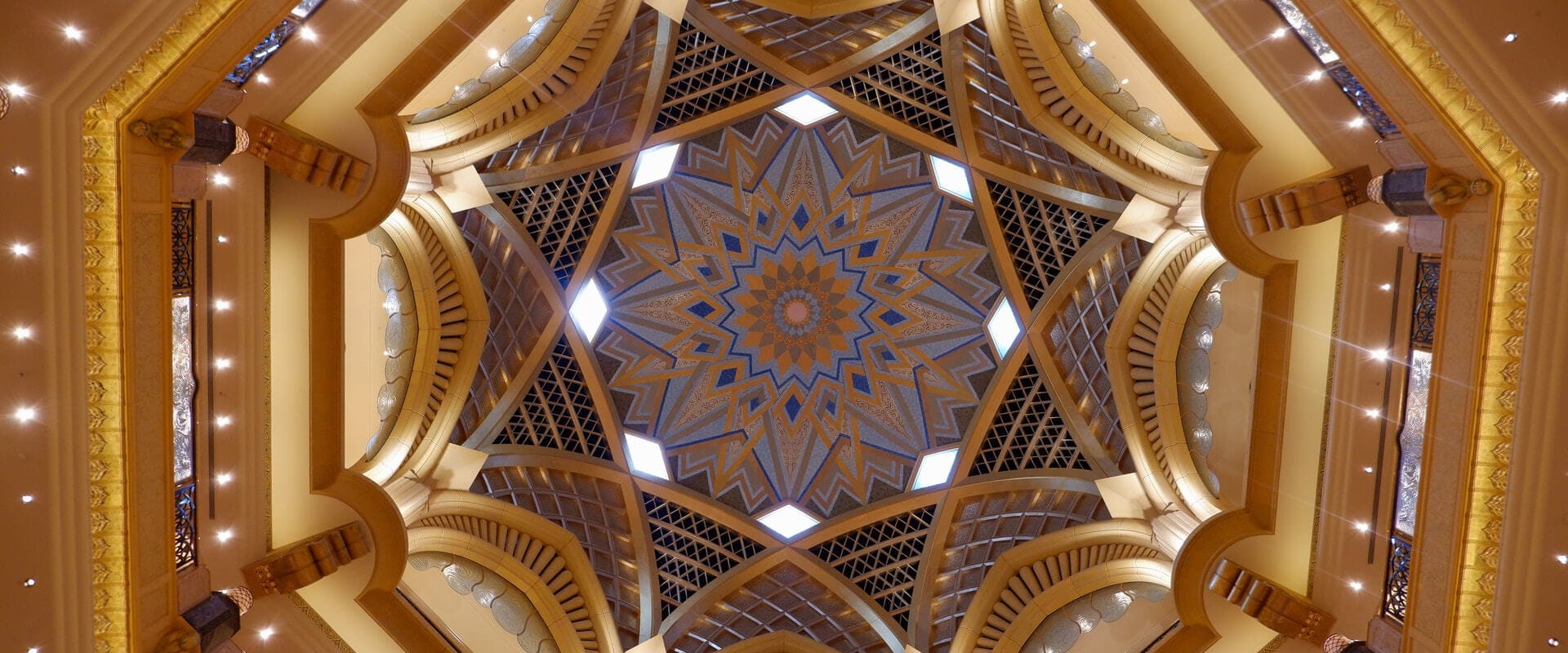 Ornate ceiling of Grand Mosque in Dubai, featuring intricate geometric patterns and luxurious chandeliers.
